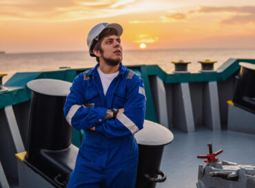 Marine Deck Officer or Chief mate on deck of offshore vessel or ship , wearing PPE personal protective equipment - helmet, coverall. Sunset light